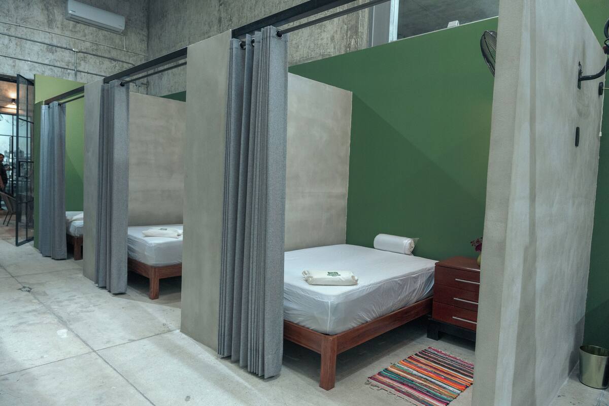 A hotel room with a bed, a wooden dresser, a small table, and a green wall.