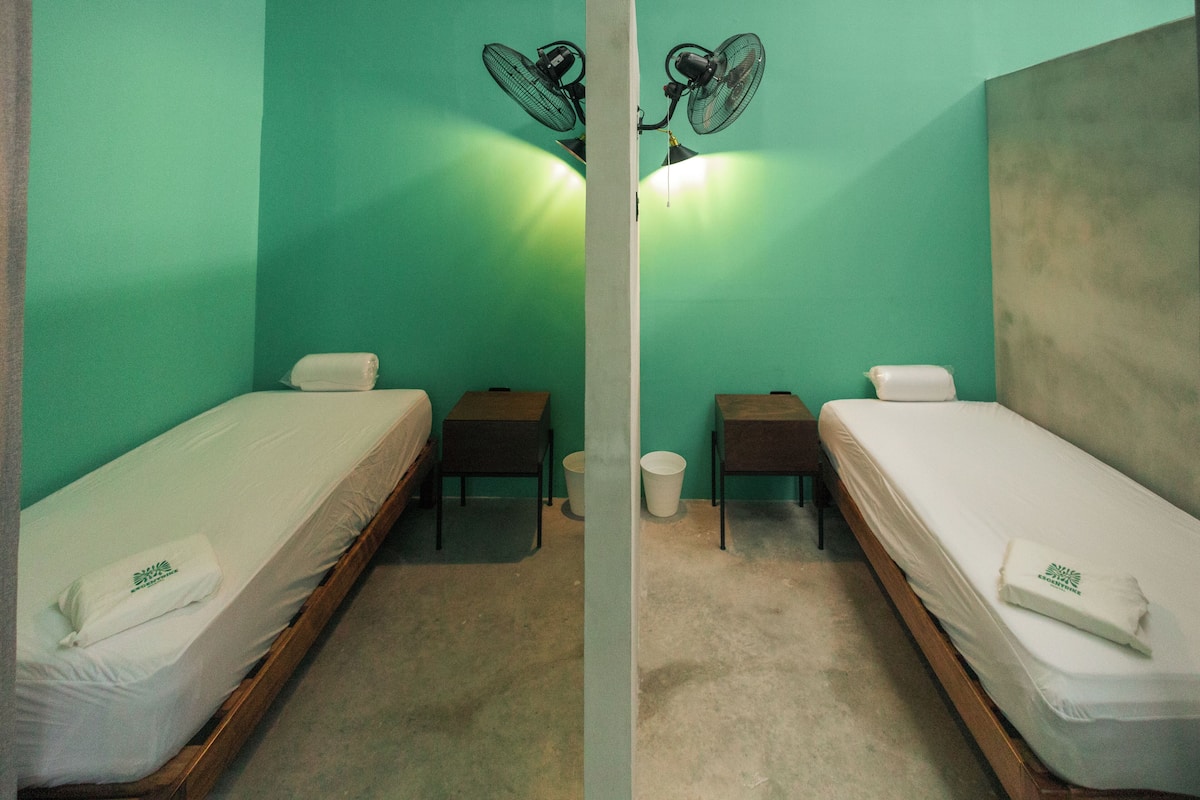 A room with two single beds, each with a pillow and a small table beside.