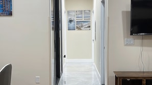 A hallway with a wooden floor, a television mounted on the wall, and a door at the end.