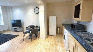 A modern kitchen with wooden flooring, a dining area with a table and chairs, a refrigerator, a microwave, and wooden cabinets. - Spacious flat in the East End

 (London)