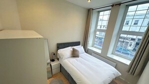 A bedroom with a bed, a nightstand, a lamp, and a window with curtains. - Spacious flat in the East End

 (London)