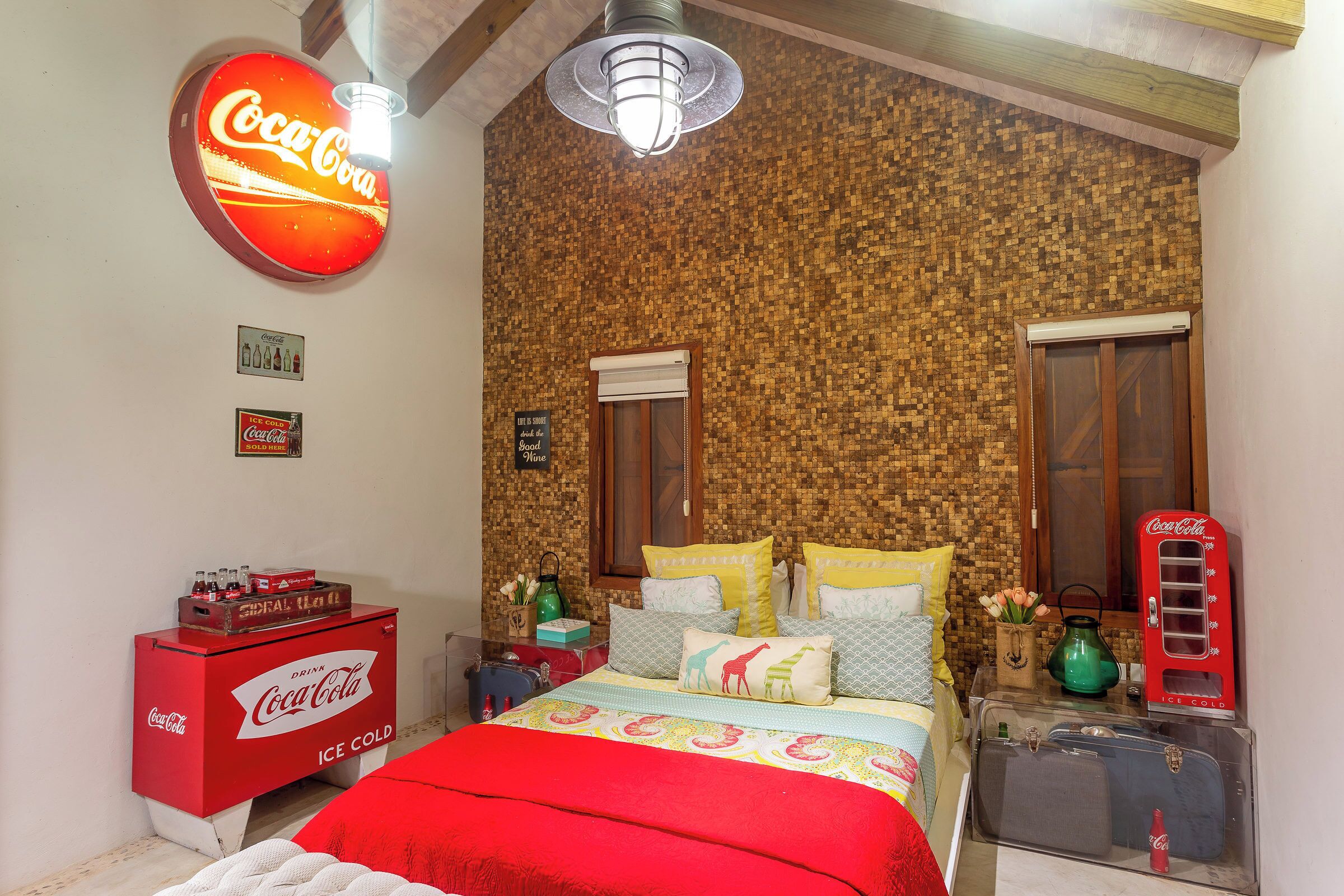 A room with a Coca-Cola branded ice cooler, a vintage Coca-Cola phone, and a bed with colorful bedding.