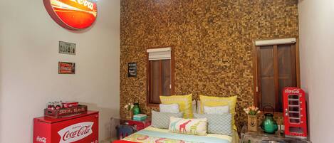 A room with a Coca-Cola branded ice cooler, a vintage Coca-Cola phone, and a bed with colorful bedding.