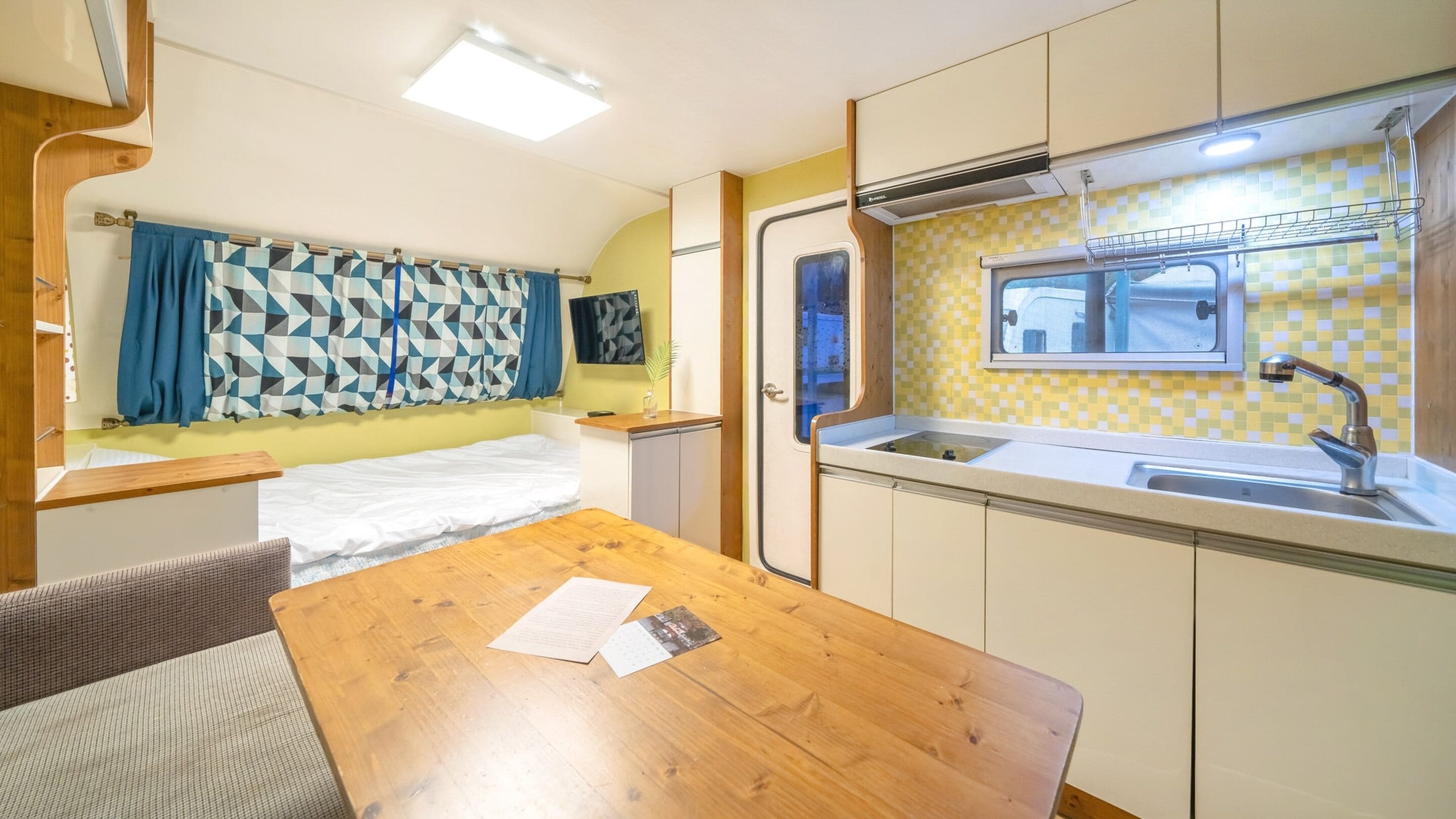 A compact RV kitchen with a sink, a small window, and a dining area with a table and chairs.