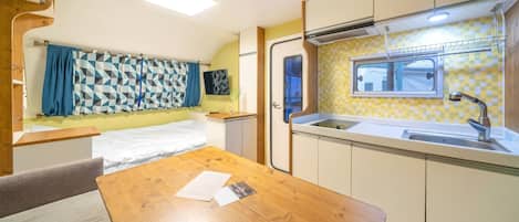 A compact RV kitchen with a sink, a small window, and a dining area with a table and chairs.