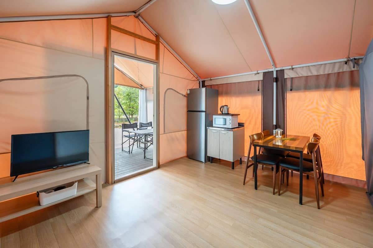 Une tente compacte et bien éclairée, équipée d’une kitchenette, d’un coin repas et d’un téléviseur.