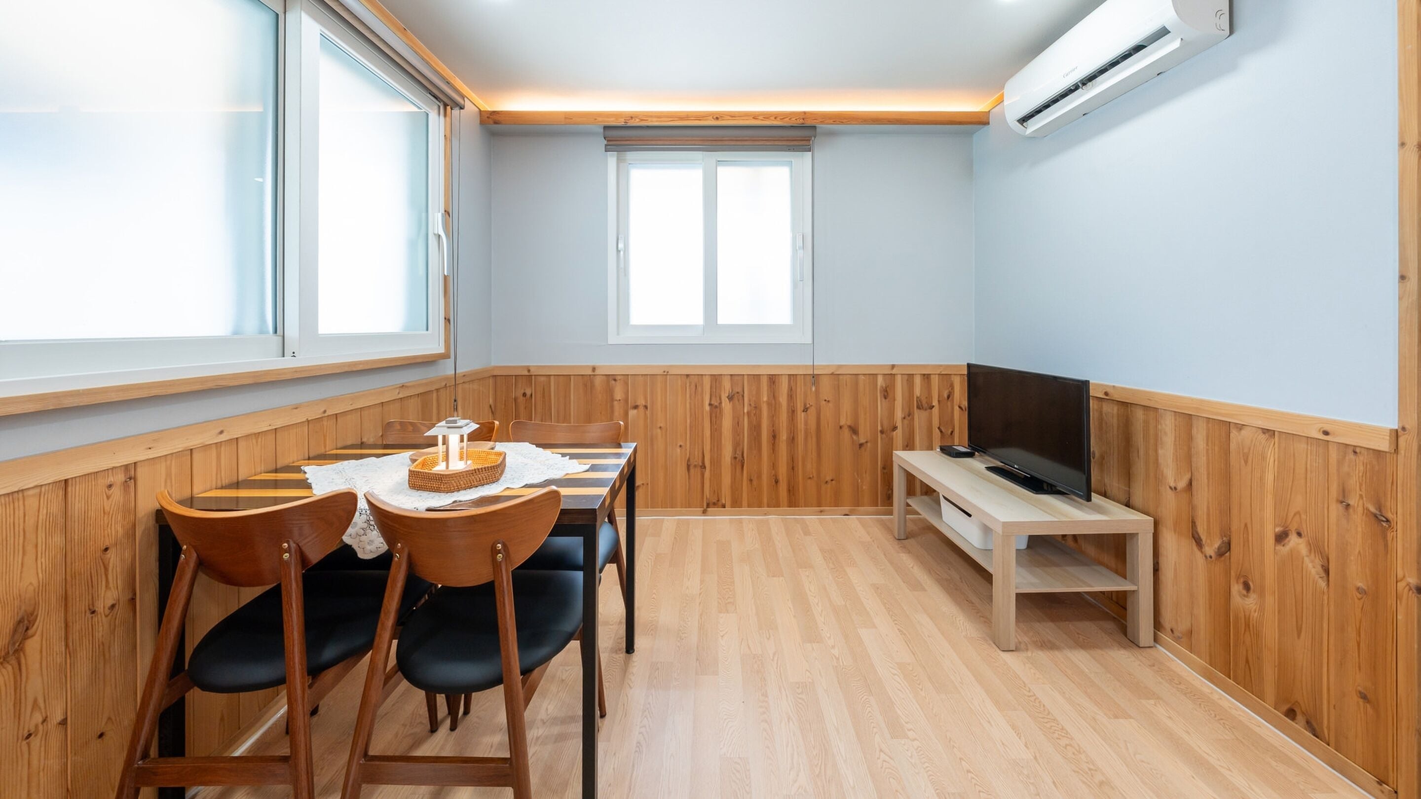 A room with a dining table, chairs, a TV, and an air conditioning unit.