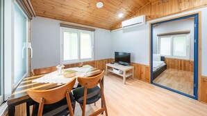 A room with a wooden ceiling, a TV on a wooden stand, a dining table with chairs, and a bed with a window. - Gapeyong Fourseason Pet Glamping Caravan (Gapyeong)