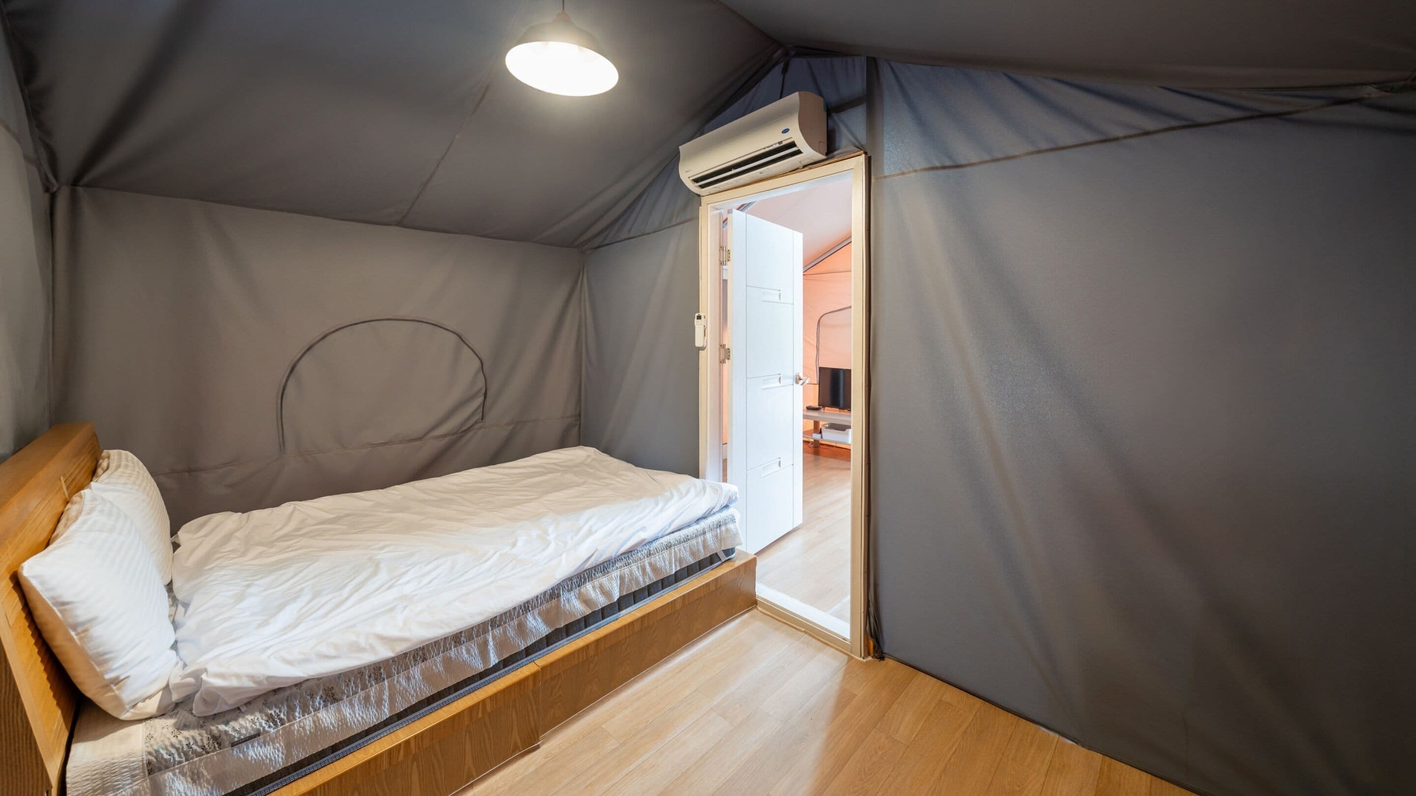 Une petite pièce comprenant un lit, un appareil de climatisation et une porte donnant sur une autre pièce.