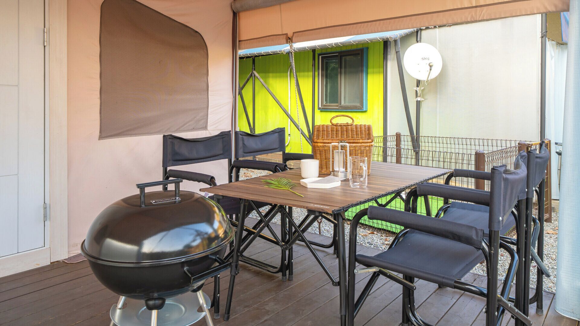 Un patio exterior con una parrilla, una mesa, sillas y una cesta de mimbre.