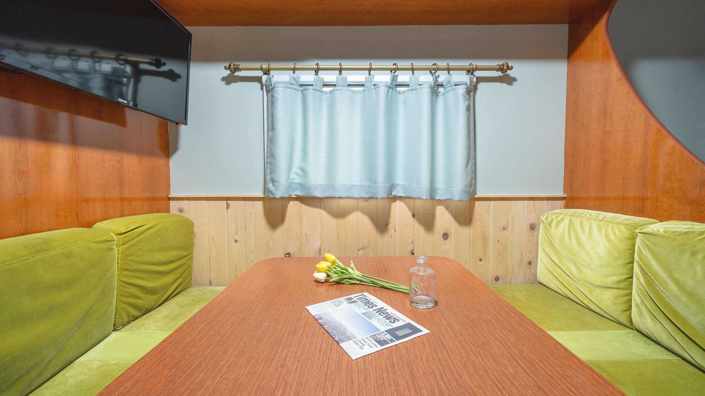 A cozy room with a wooden table, two green sofas, a light blue curtain, and a newspaper.
