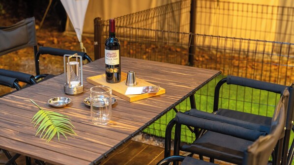 An outdoor dining table with a bottle of wine, glasses, and a menu.