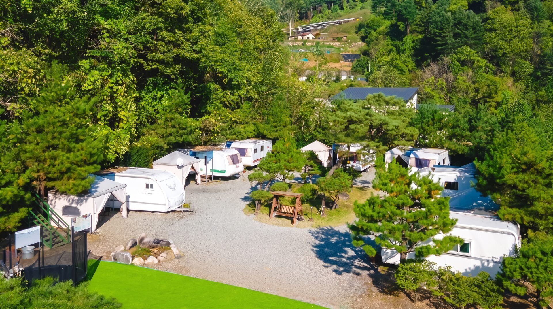 Un camping con vehículos recreativos y casas móviles, rodeado de árboles densos.