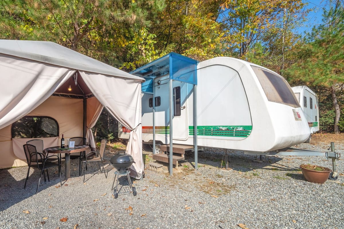 Un espace de camping comprenant une tente, une table avec des chaises, un barbecue et un véhicule récréatif.