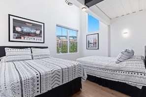 A hotel room with two beds, a large window, and a framed picture of a stadium.