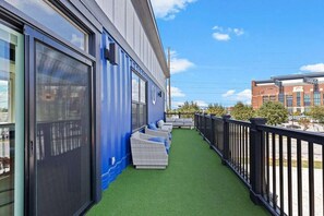 A balcony with artificial grass, outdoor seating, and a view of the cityscape.