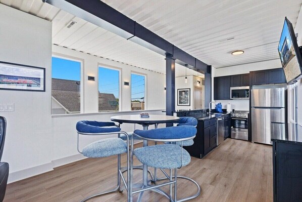 A modern kitchen with stainless steel appliances, a dining area with blue bar stools, and a large window offering a view of the outside.