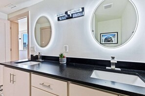 Bathroom features two sinks, a potted plant, and a door to a separate room.