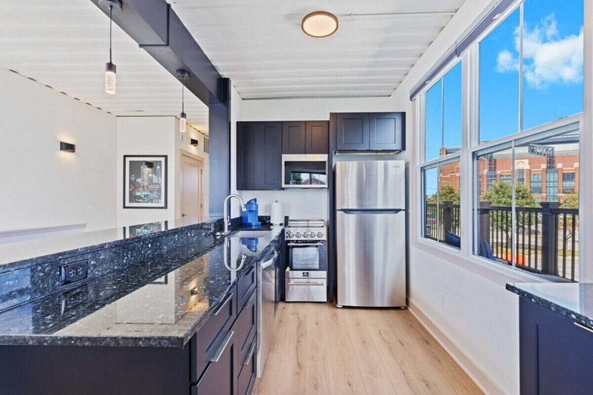 A modern kitchen with dark cabinetry, stainless steel appliances, and a large window offering a view of the city.