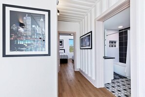 A hallway with framed cityscape pictures, a wooden floor, and a tiled bathroom area.