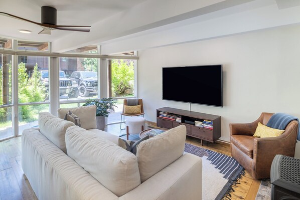 Una sala de estar moderna con un sofá grande, un sillón de cuero, un televisor de pantalla plana y una estantería.