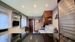 Eine moderne Küche mit eingebautem Ofen, ein Essbereich mit Tisch und Stühlen sowie ein Wohnzimmer mit Sofa und Fernseher.