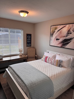 A bedroom with a bed, a chair, a window with blinds, a wall-mounted light fixture, and a framed inspirational quote. - Charming 3-bedroom Home in Canby (Canby)