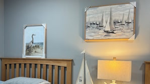 A bedroom with a bed, a nightstand with a lamp, and two framed artworks on the wall.