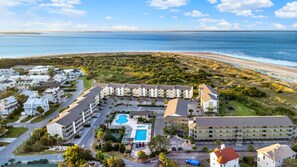 Luchtfoto van een kusthotel met meerdere gebouwen, een zwembad en een strand op de achtergrond.