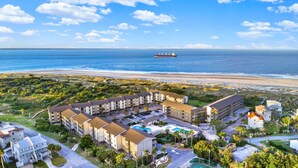 Un hotel a la costa amb diversos edificis, una platja i un vaixell a la distància.