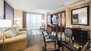 A hotel room with a sofa, a glass table with chairs, a TV, and a large window with curtains. - SVS: 1BD/2BA Mountain View | Private Balcony | Pool & Gym | Signature at MGM (Las Vegas)