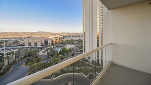 A high-rise hotel room with a balcony overlooking a cityscape, including a large building and palm trees. - SVS: 1BD/2BA Mountain View | Private Balcony | Pool & Gym | Signature at MGM (Las Vegas)