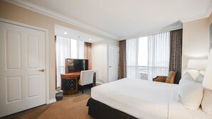 A hotel room with a large bed, a desk with a television, and a view of the city through the windows. - SVS: 1BD/2BA Mountain View | Private Balcony | Pool & Gym | Signature at MGM (Las Vegas)