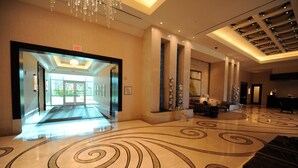 Un hall d’hôtel spacieux, agrémenté d’un imposant lustre, d’un sol à motifs et d’un panneau de signalisation indiquant clairement la sortie.