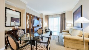 Une chambre d’hôtel comprenant un coin repas, un canapé, une télévision et une grande fenêtre avec des rideaux.