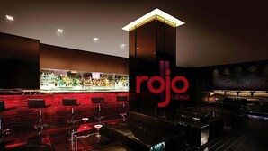 Un área de bar con alfombra roja, taburetes y una barra bien iluminada.