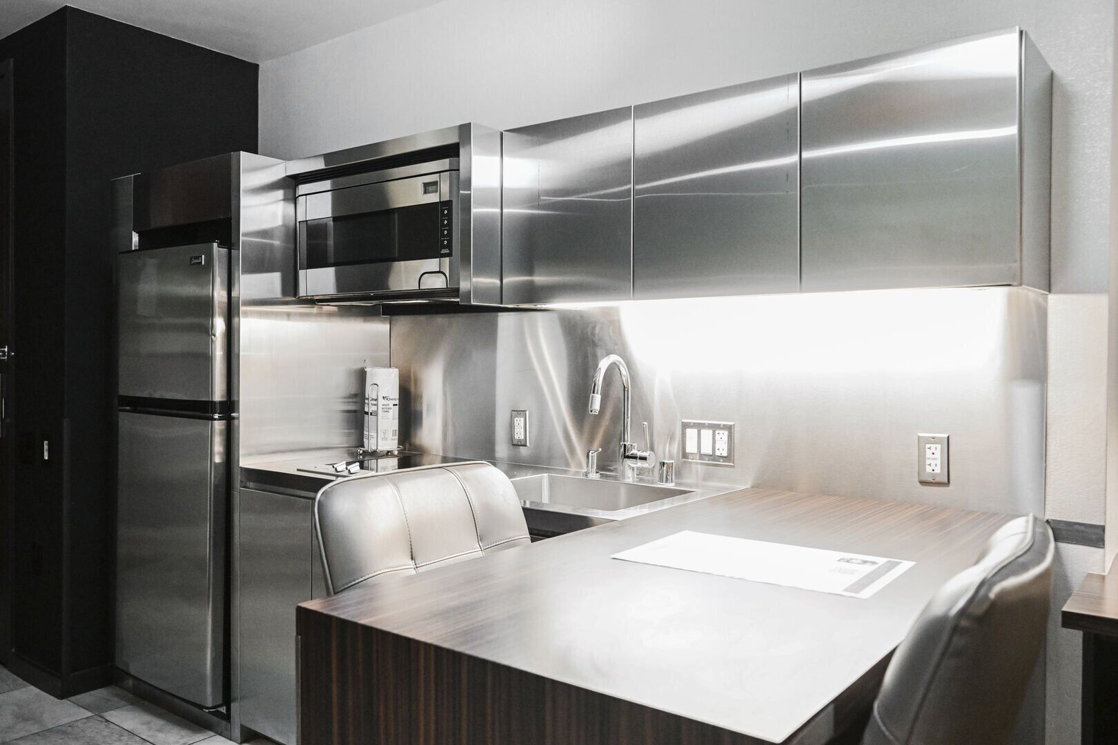 A modern kitchen with stainless steel appliances, a wooden dining table, and a built-in microwave.