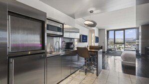 A modern kitchen with stainless steel appliances, a dining area with bar stools, and a large window offering a city view.
