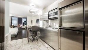 A modern kitchen with stainless steel appliances, a dining area with a bar stool, and a view of the city at night. - SVS: High Floor Strip View Studio | Open Balcony | Palms Place (Las Vegas)