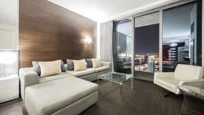 A modern hotel room with a sofa set, a glass coffee table, and a view of a cityscape at night. - SVS: High Floor Strip View Studio | Open Balcony | Palms Place (Las Vegas)
