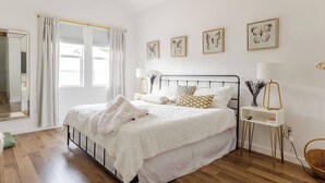 A bedroom with a bed, bedside tables, a mirror, and artwork on the wall.