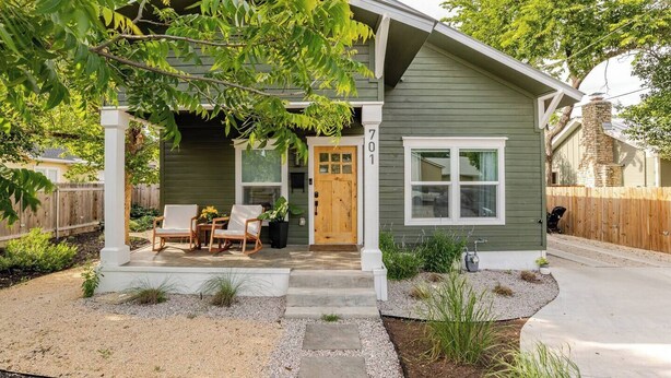 A single-story house with a front porch, a wooden door, and a small garden area with a patio table and chairs.