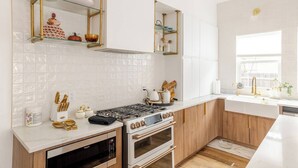 A modern kitchen with white cabinetry, a gas stove, an oven, and a window providing natural light.
