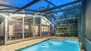 A pool area with a glass enclosure, a red chair, and a table with an umbrella. - Tropical Retreat | Private Pool, 1 Block to Siesta Key Beach, Quick Access to Village! (Siesta Key)