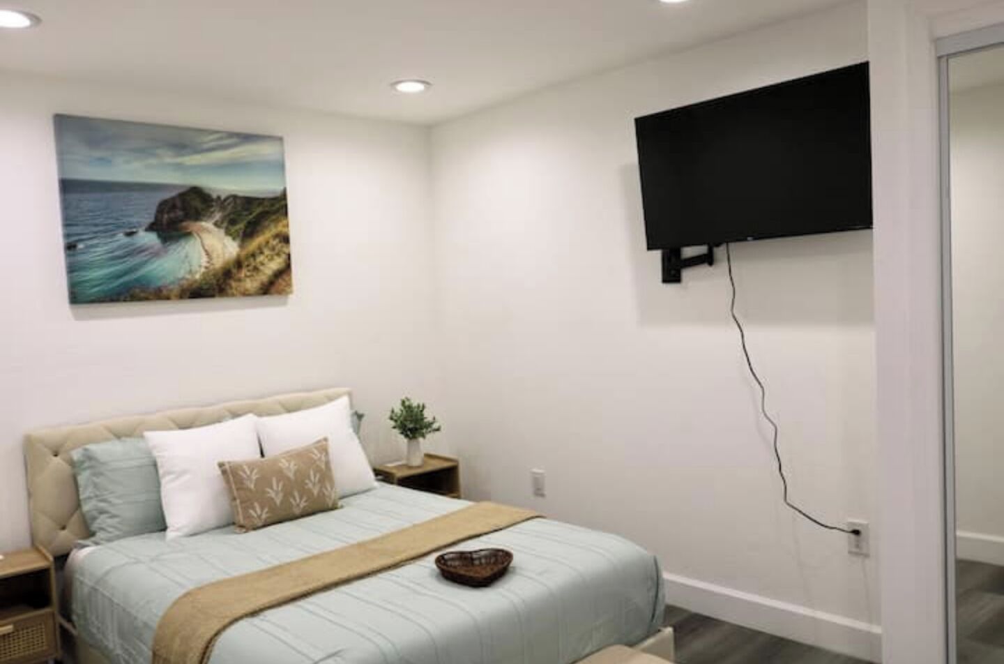 Un dormitorio con cama, televisor montado en la pared y un cuadro de un perro en un acantilado.
