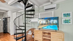 A modern living room with a spiral staircase, a flat-screen TV, and a wooden cabinet. - 🌴 Palm Shade Cottage | Charming 1-Bedroom in SK, Access to Pool, Walk to Beach! (Siesta Key)