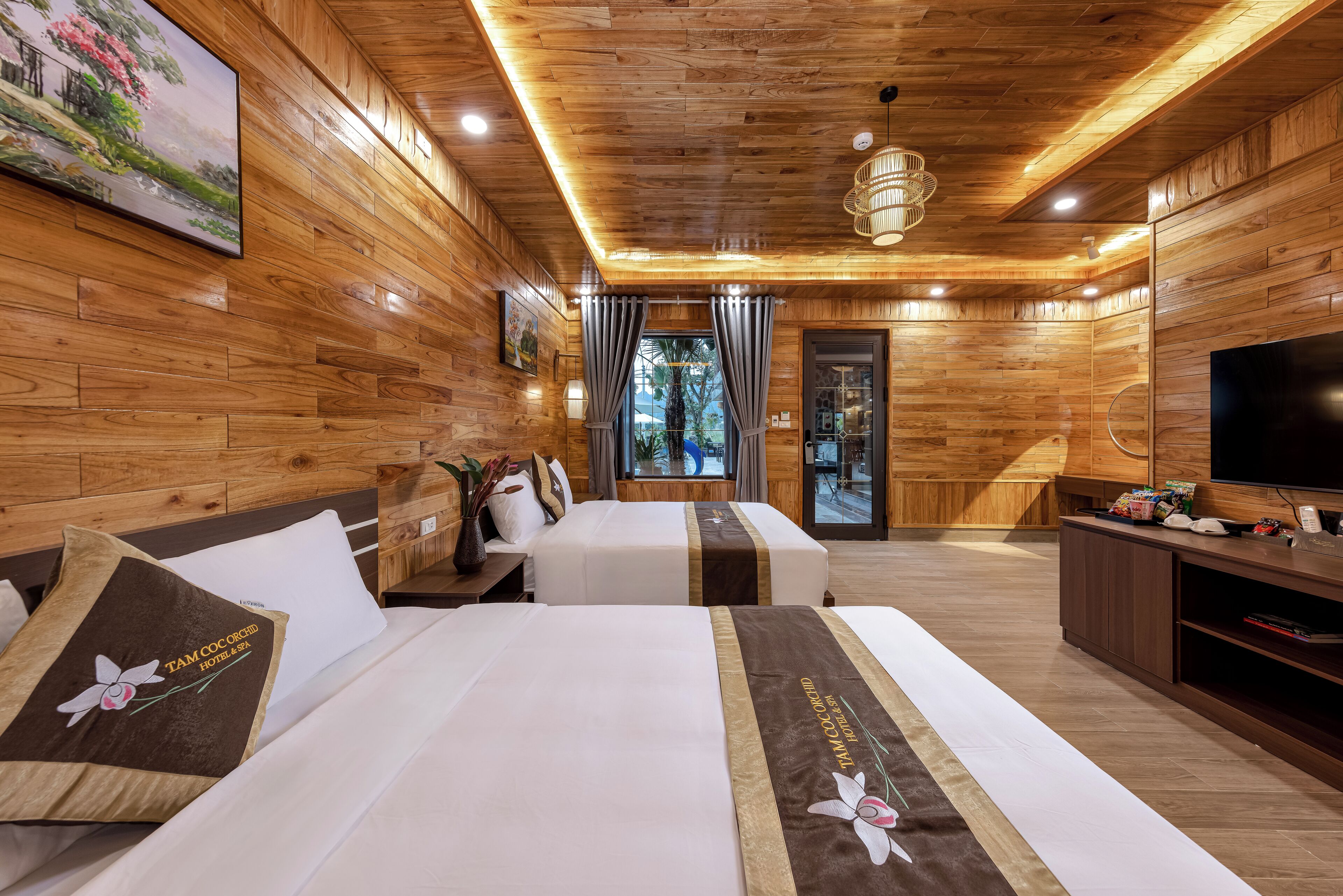 A wooden-themed hotel room with two beds, a TV, and a view of the outdoors.