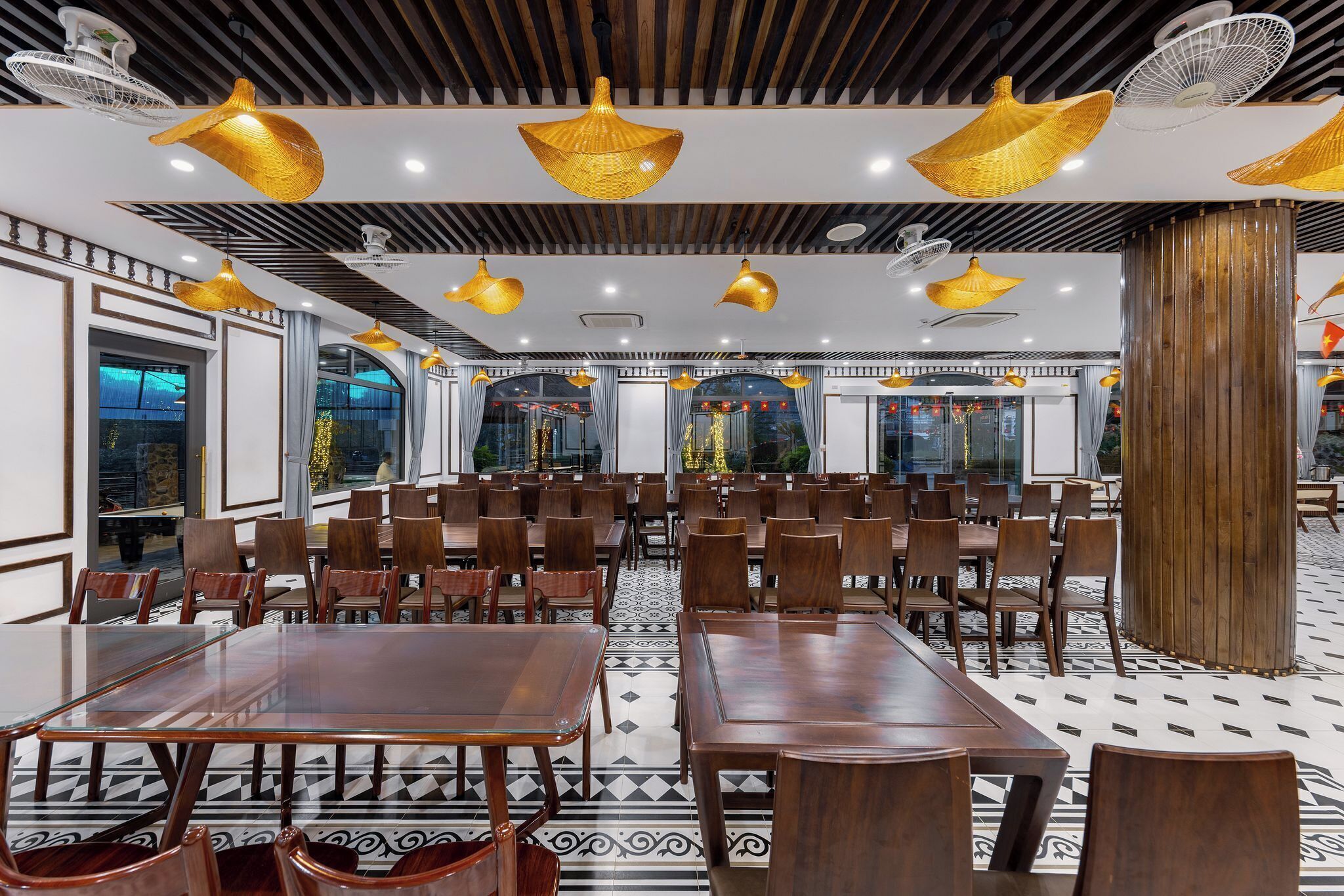 A spacious dining area with wooden tables and chairs, large windows, and decorative ceiling fans.