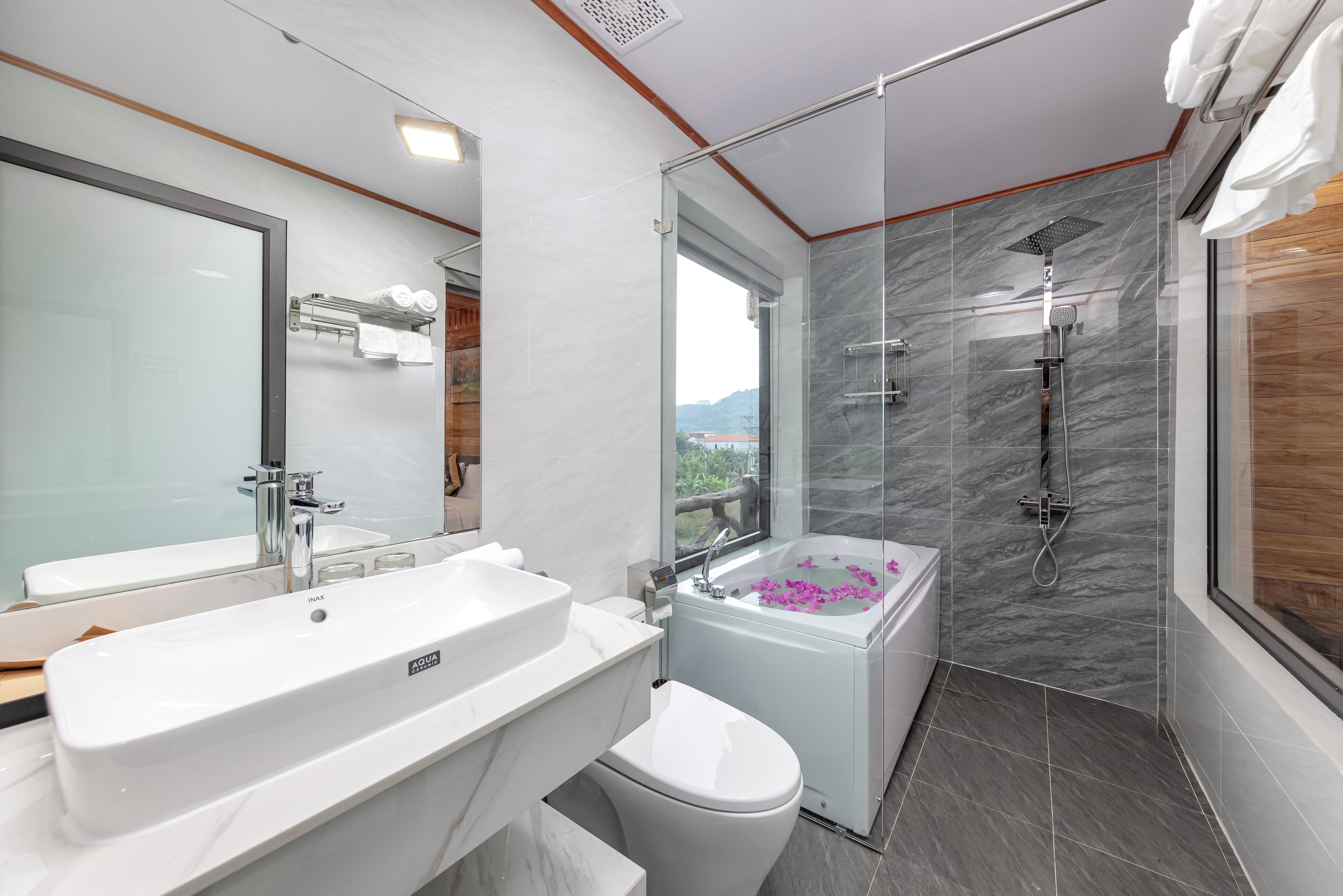 A modern bathroom with a large white sink, a toilet, a bathtub with rose petals, and a shower with a glass enclosure.