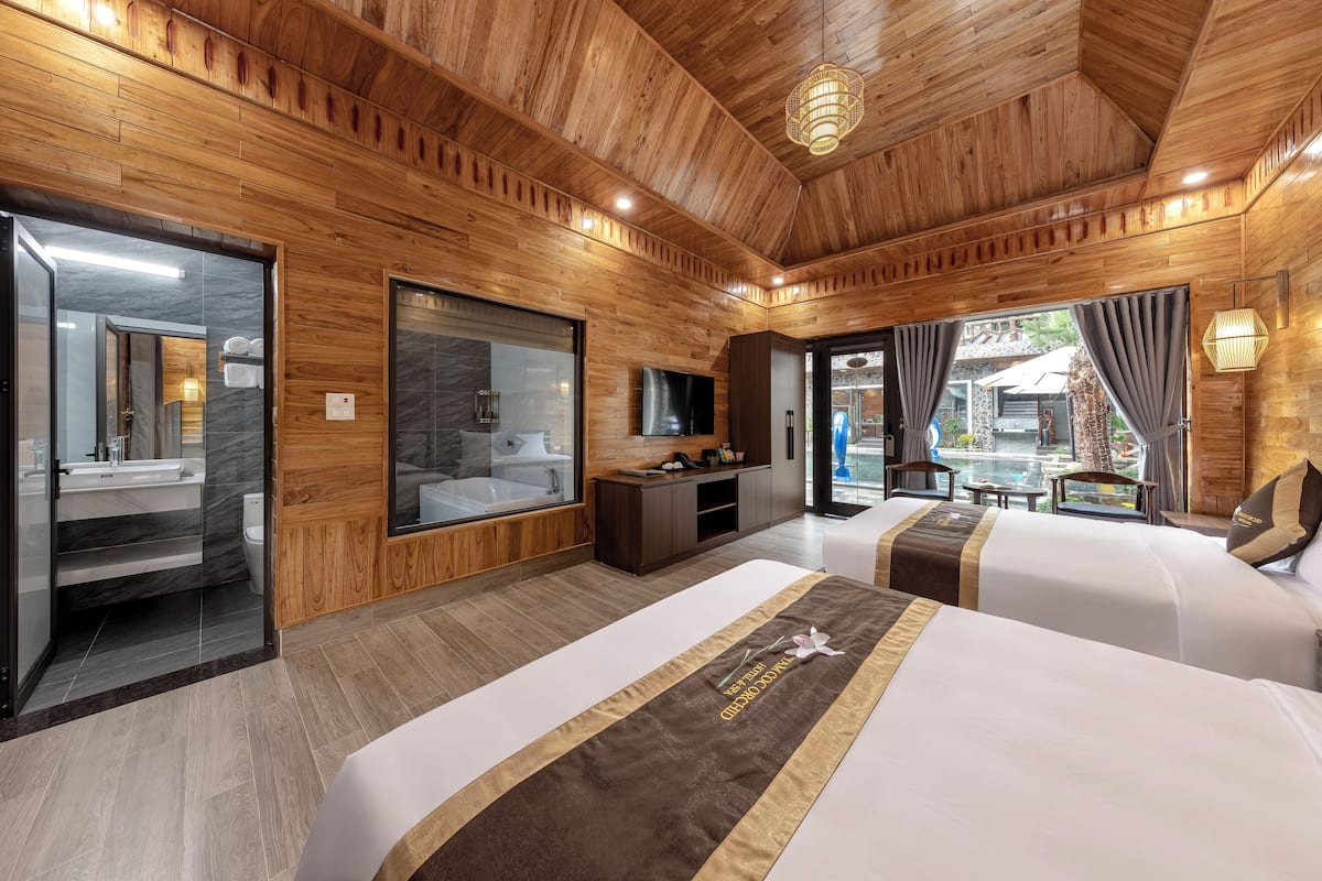 Une chambre d’hôtel avec des boiseries, un grand miroir, une télévision, deux lits, un bureau et une vue sur l’extérieur.